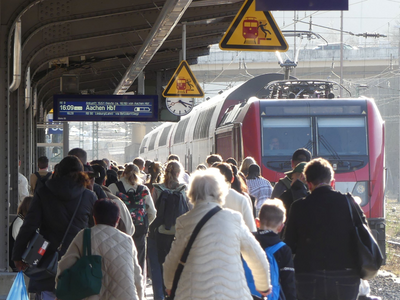 Reisende gehen auf einem Bahnsteig zu einem haltenden Reisezug