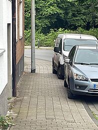 Autos parken teilweise auf dem Gehweg, sodass zwischen der Laterne und dem Auto etwa ein halber Meter frei bleibt.