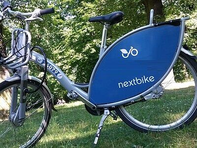 Ein Nextbike-Fahrrad steht auf einer Wiese. Im Hintergrund sind Bäume