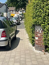Ein Auto parkt teilweise auf einem Gehweg, soadss weniger als ein Meter Gehweg frei bleibt.